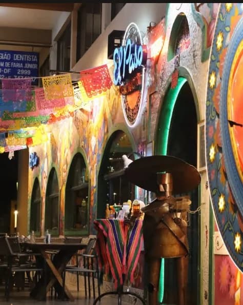 Entrada do El Paso Asa Norte à noite, com letreiro luminoso, papel picado, murais e estátua de mariachi